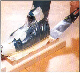5 Cubra la caja del taladro con un plástico y coloque el taladro en la masilla suave. Fije el taladro firmemente entre las tiras en el bloque de soporte.